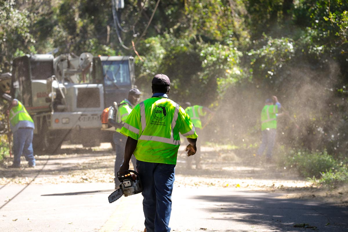 Public works employee carrying chainsaw an walking toward debris cleanup site along a roadway
